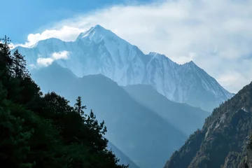 Photo sur Plexiglas Manaslu View on Himalayas, Annapurna Circuit Trek, Nepal. The view is disturbed by dense tree crowns in the front. High snow caped mountains peaks catching the first beams of sunlight. Serenity and calmness