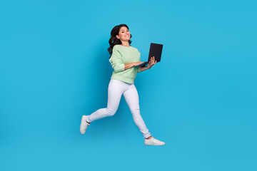 Full body photo of nice young brunette lady jump write laptop wear shirt pants sneakers isolated on blue background