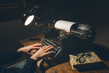 Typing hands of a writer looking for inspiration to start a new novel on his vintage typewriter in...