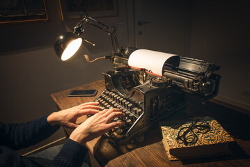 Typing hands of a writer looking for inspiration to start a new novel on his vintage typewriter in...