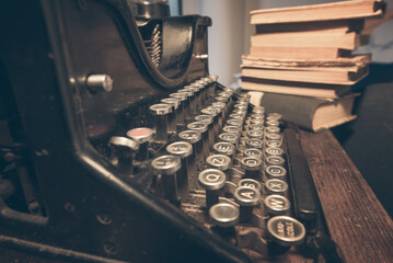 An old classic typewriter in a vintage style studio with a wooden desk lit by a lamp, wit old books all around. A moody, dark atmosphere for a writer working at night.