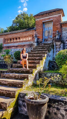 Girl sitting at the stairs leading to one of the temples in Lombok, Indonesia. She is enjoying her time and beautiful weather.  A flower pot on the side. Discovering new places, cultures and tradition