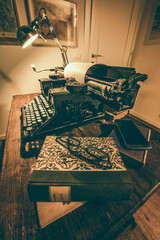 An old classic typewriter in a vintage style studio with a wooden desk lit by a lamp, wit old books all around. A moody, dark atmosphere for a writer working at night.