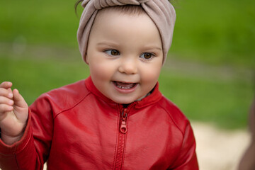 Portrait of a 2 year old girl. Girl in a red leather jacket and headband.