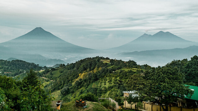Green plants on hills and Volcan de Fuego mountains on the horizon in Antigua, Guatemala