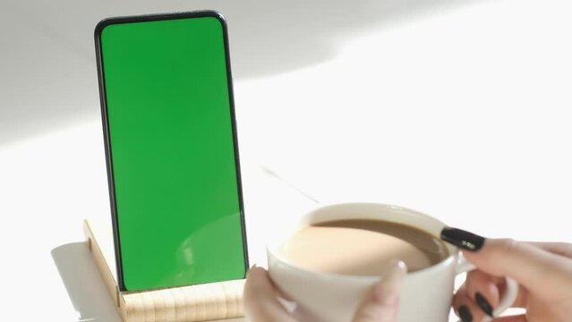 Young female hands using green screen smartphone sitting in cafe drinking coffee. Online business communication. Chroma Key mockup. Social network. Internet chatting.