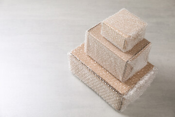 Cardboard boxes covered with bubble wrap on light grey table. Space for text