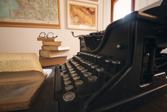 Typing hands of a writer looking for inspiration to start a new novel on his vintage typewriter in a retro style studio: a wooden desk lit by a lamp, old books and a pair of glasses.