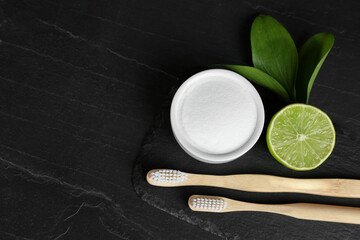 Bamboo toothbrushes, lemon and bowl of baking soda on black table, flat lay. Space for text