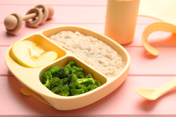 Plastic dishware with healthy baby food on pink wooden table, closeup