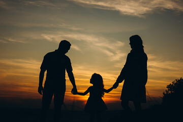Fototapeta na wymiar Silhouette of happy family on colorful sky during sunset. Happy mom dad daughter family moment outdoors in the park.