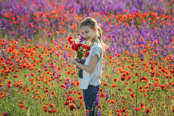 Naklejka premium Little girl holding big bouquet with poppies on the background of a colorful spring field