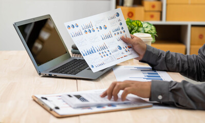 close up of businessman hand working on laptop computer with business graph information diagram on wooden desk as concept