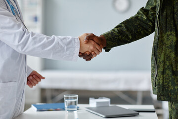 Unrecognizable African American military man and Caucasian doctor in lab coat doing handshake...