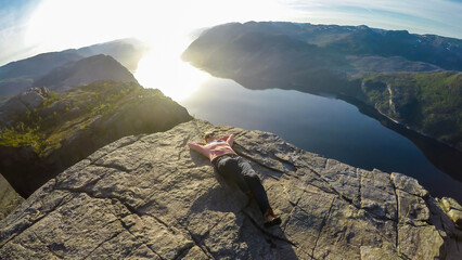 A girl lying at the edge of a steep cliff of Preikestolen, with a view on Lysefjorden. The girl...