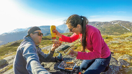 A couple having a grill in the tall mountains. Few sausages are being grilled. Couple uses portable...