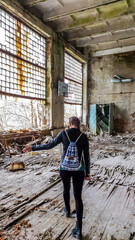 Obraz na płótnie Canvas Girl in black outfit walks around the rotten floor in an abandoned sports hall in Pripyat, Ukraine, after the Chernobyl explosion. The floor is completely rotten. Lots of decaying object on the floor