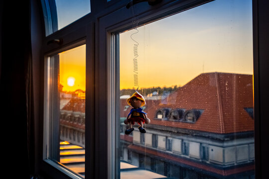 Closeup of a small Pinoccio doll hangin on a window on a view of the sunset