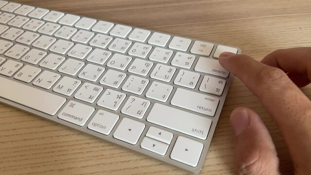 Typing on keyboard. Male hand fingers pressing "delete" button key on English - Thai computer white keyboard close up shot. Work from home professional hand press backspace button to delete text