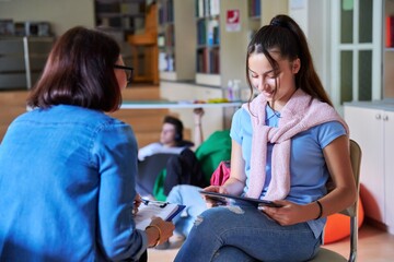 Teenage girl student talking with teacher mentor in the library.