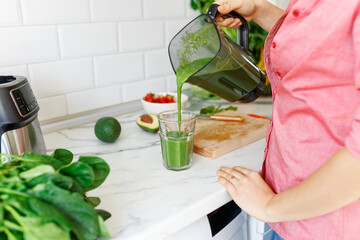 Closeup housewife pours ready green smoothie. Healthy food.Happy woman on detox diet, pouring green...