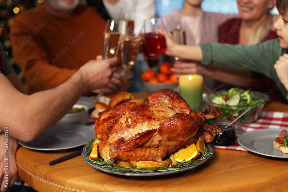 Wall mural Family clinking glasses of drinks at festive dinner, focus on delicious baked turkey. Christmas celebration