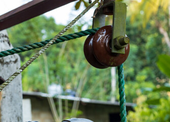 A brown pully and a green rope on it with a green garden in the background