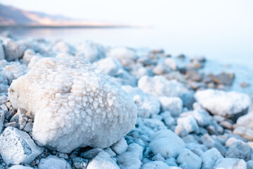 Desert rocky shore of Dead Sea. Stones on beach covered with white salt crystals. Exotic seaside landscape. Miracle, magic and mystery of nature