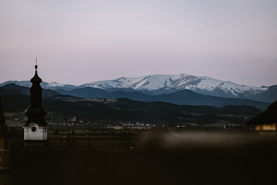 Church with partially snowed Krizna peak in the background in Zvolen city during blue hour