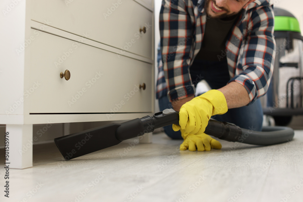 Wall mural Man vacuuming floor under chest of drawers indoors, closeup