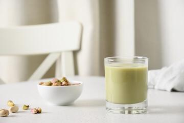 Obraz na płótnie Canvas Pistachio milk in glass and pistachios in glass jar on white kitchen background. Lactose free. Vegan nutty plant based milk. Vertical.