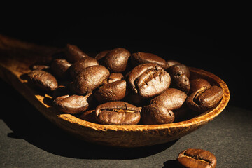 Close-up coffee beans in wooden spoon on black background.