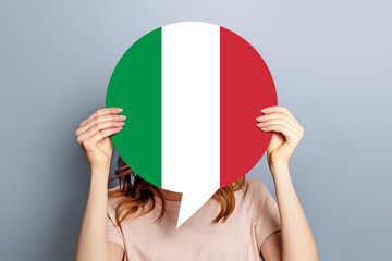 Student girl holds blank white speech bubble with italian flag isolated over grey studio...