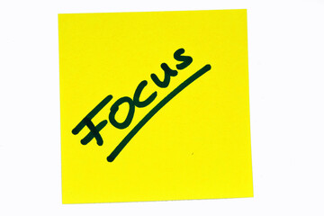 Black colored inspirational motivating quote "Focus" on a yellow post-it over a white background