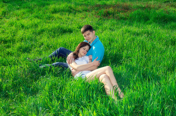 Naklejka na ściany i meble The girl lies on the knees of the guy among the green grass.