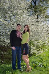 A young loving couple man and woman in embroidered shirts near a flowering tree in a spring garden.