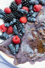 Purple crepes with berries and syrup