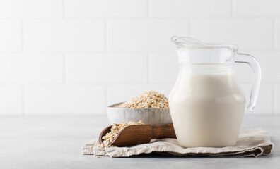 A jug of oat milk, a bowl of oatmeal on the table on a light background. Copy space.
