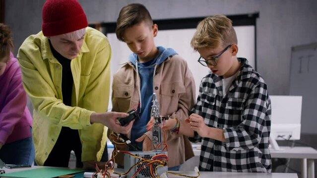 Kids with teacher working together on project with electric toys and robots at robotics classroom