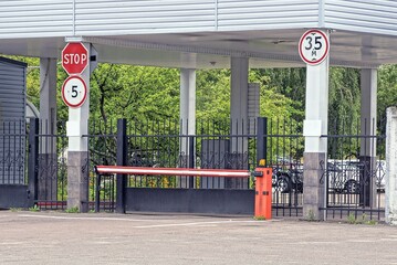 red white closed automatic barrier on the street at the checkpoint with black iron gates and a metal fence with traffic signs