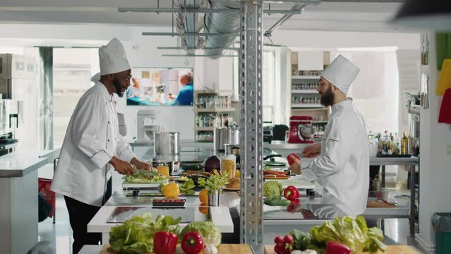 Diverse team of chefs preparing ingredients for culinary recipe, cutting vegetables and cooking gourmet meal. Cheerful people making authentic food dish in professional restaurant kitchen.