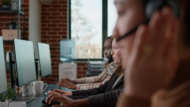 Group of people answering helpline calls at customer support service, giving assistance about telemarketing. Call center workers using headset to give telesales support, looking at computer.
