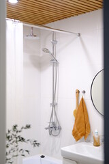 Stylish bright bathroom with sink and round mirror. Rain shower head in bathtub