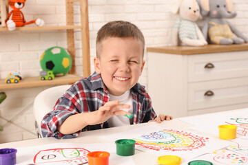 Little boy painting with finger at white table indoors