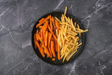 Black plate filled half and half of sweet potato fries and French fries, flat lay