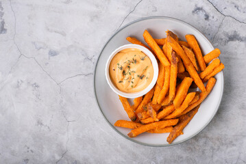 Baked sweet potato fries on a plate with savory sauce over concrete background, top view - obrazy, fototapety, plakaty