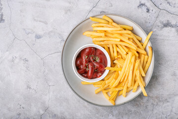 French fries with ketchup on a plate over concrete background, top view