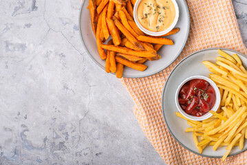 Baked sweet potato fries and French fries on plates over concrete background, top view