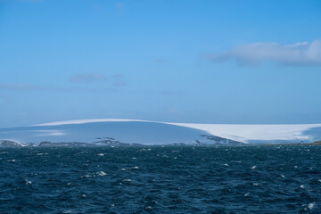 Huge hills covered in snow and ice and the Antarctic ocean visible in the distance