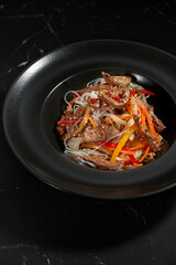 Funchoza with beef and vegetables on a black background, top view, copy space. Glass noodles, Asian food.